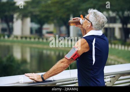 Senior sporty man standing on the bridge and drinking water Stock Photo