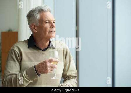Pensive aged man looking through the window and drinking wine Stock Photo