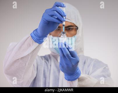 There will be no contaminations on my watch. a medical professional standing in a disposable hazmat suit and using a syringe to prepare a Covid Stock Photo