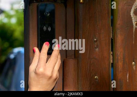 Woman's hand pressing a doorbell on a wooden fence in the garden Stock Photo