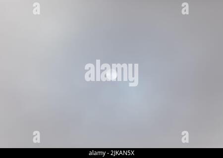 Full frame of unclear sky with midday sun in the middle shinning through a thick veil of dense grey clouds Stock Photo
