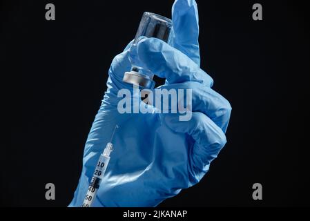 the doctor's hands hold a syringe of liquid vaccine against a black background. Close-up of the vial and syringe Stock Photo