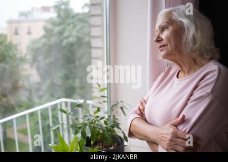 An elderly woman looks sadly out the window. Stock Photo