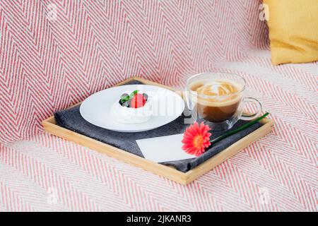 Cup of coffee, Pavlova dessert cake, gerbera flower and blank postcard with copy space on the tray with gray napkin. Breakfast for loved one. Romantic Stock Photo
