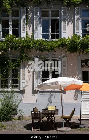 Atmospheric and romantic light pink painted facade of a house with arched windows, shutters, wisteria covered walls and outdoor terrace with parasols Stock Photo
