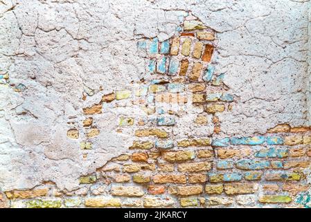 Old brick wall with patches of blue and yellow plaster paint Stock Photo