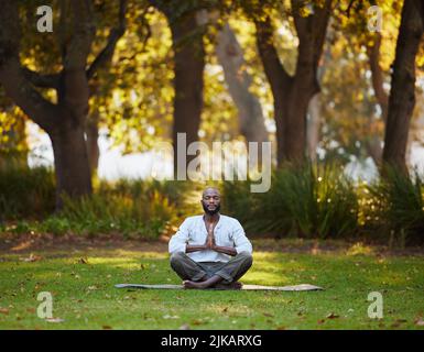 The perfect place to find your center. Full length shot of a handsome young man meditating while practicing yoga outside at the park. Stock Photo