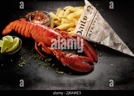 From above tasty red lobster and potato chips in newspaper sheet wrapping served on black table near lime pieces and sauce Stock Photo