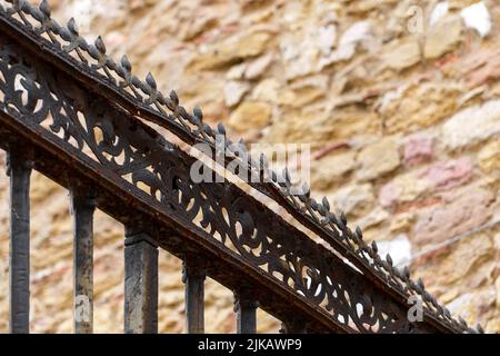 Black patterned forged iron fence with spikes and peaks of an antique medieval cathedral with a weathered stone wall in blur. Security concept Stock Photo