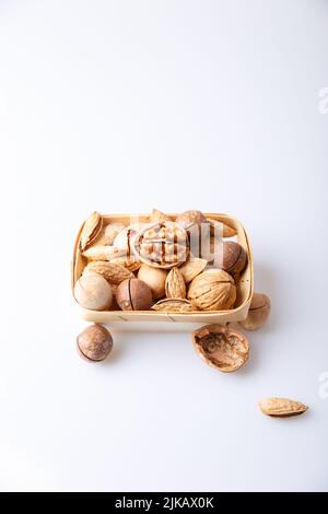 Assorted nuts in the shell on a white background: walnuts, pecans, almonds, macadamia. Nuts in a basket. Selective focus, close-up. Place for text. Stock Photo