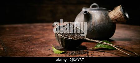 Heap of loose tea on table with fresh green leaves for brewing placed on wooden table with vintage metal teapot Stock Photo