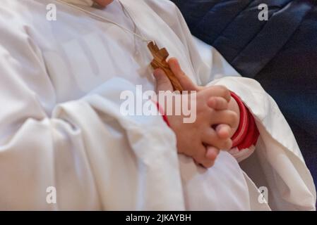 Italy, May 2022, Child's hands play with the cross that was given to him on the day of his first communion Stock Photo