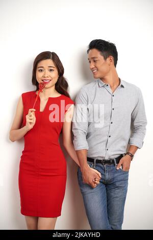 Portrait of beautiful Asian couple holding hands while posing near wall on Valentines day Stock Photo