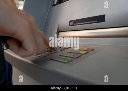 Woman's hand is typing a PIN code on the keyboard of a modern ATM in a shopping center. Selective focus Stock Photo