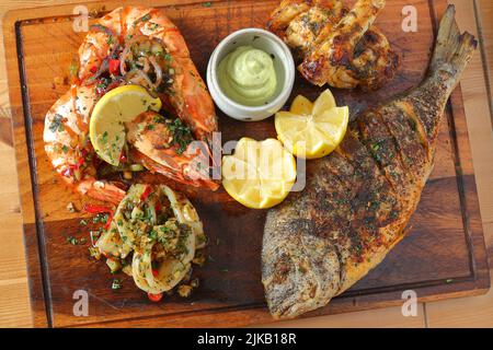 Mixed seafood platter with tiger prawns, calamari and whole grilled fish garnished with lemon and sauce Stock Photo