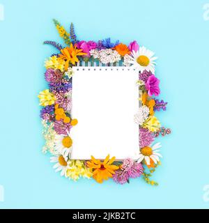 Summer minimal layout made with white blank spiral notebook and colorful flowers on blue background. Mock up in flat style. Top view. Stock Photo