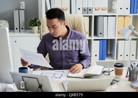 Young Asian architect analyzing blueprints of apartments Stock Photo