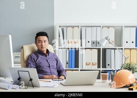 Confident young Vietnamese engineer sitting at his table in office Stock Photo
