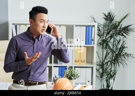 Young Vietnamese engineer talking on the phone with client Stock Photo