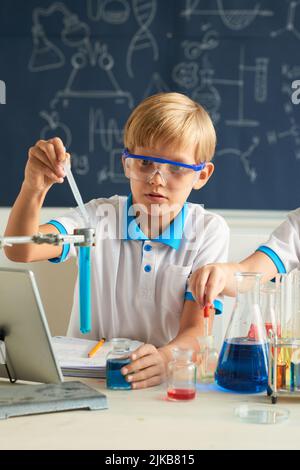 Schoolboy in goggles conducting experiment with chemical liquids Stock Photo