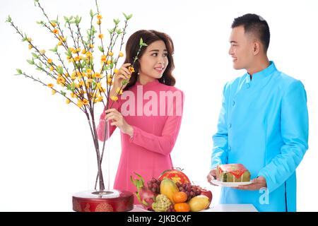 Cheerful young amn bringing traditional dishes when his girlfriend decorating atble for Tet celebration Stock Photo
