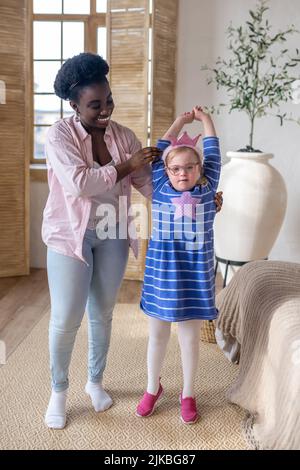 Smiling dark-skinned lady having good time with a cute girl in blue dress Stock Photo