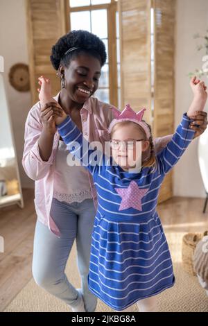 Smiling dark-skinned lady having good time with a cute girl in blue dress Stock Photo