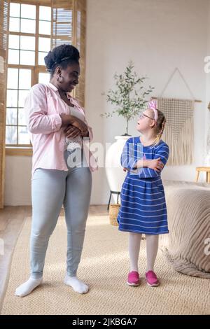 Smiling dark-skinned lady having good time with a cute girl in blue dress Stock Photo