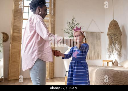 Smiling dark-skinned lady having good time with a cute girl in blue dress Stock Photo