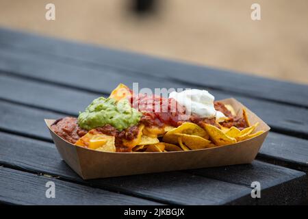 Portion of street food, chilli and cheese nachos with guacamole, salsa and sour cream topping Stock Photo