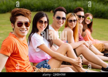 Cheerful young Vietnamese people resting in the park, focus on smiling guy Stock Photo