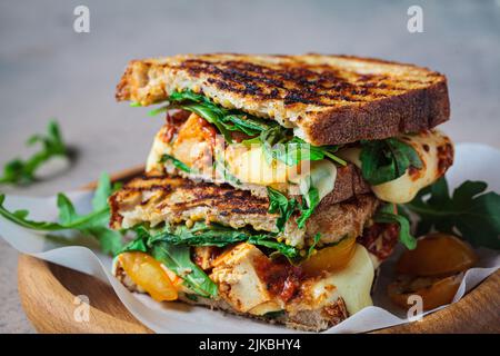 Grilled sandwich with vegetables and mozzarella on a wooden board. Stock Photo