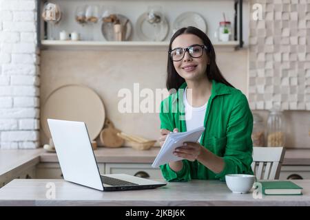 Young woman takes notes in front of laptop at home. Working from home. Concept of education and communication. High quality photo Stock Photo