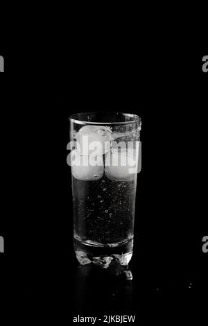Ice cubes thrown to a glass of water from above with splash on a black ...