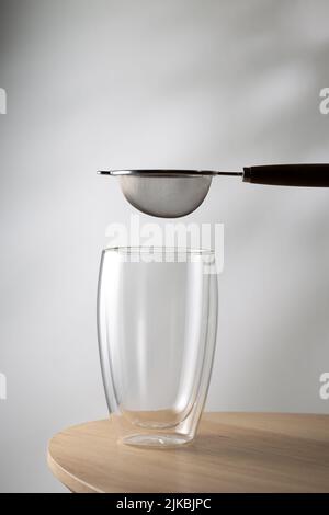 Mini strainer stainless steel and empty glass on wooden table Stock Photo