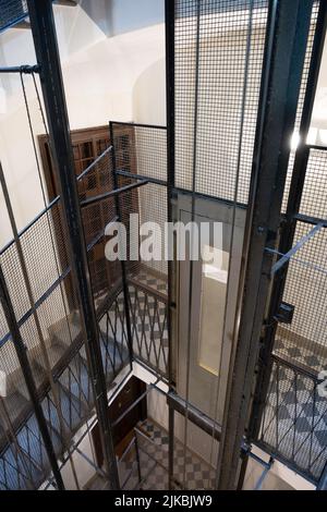 Older elevator shaft with metal frame, fencing, cables and elevator doors in a vintage apartment building. Narrow depth of field Stock Photo