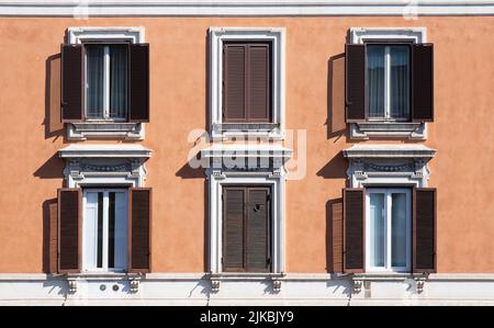 Shuttered windows, some closed, in an apartment building with an orange plastered wall on a sunny day in Rome, Italy Stock Photo