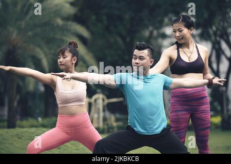 Smiling female yoga instructor correcting position of people practicing warrior asana Stock Photo