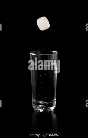 Ice cubes thrown to a glass of water from above with splash on a black ...