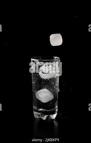 Ice cubes thrown to a glass of water from above with splash on a black ...