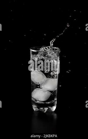 Ice cubes thrown to a glass of water from above with splash on a black ...
