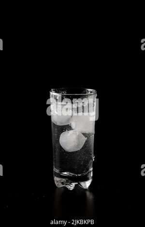 Ice cubes thrown to a glass of water from above with splash on a black ...