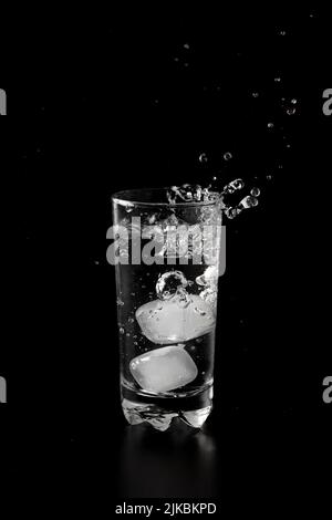 Ice cubes thrown to a glass of water from above with splash on a black ...