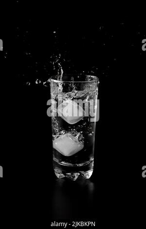 Ice cubes thrown to a glass of water from above with splash on a black ...
