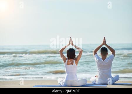 Rear view of young couple enjoying yoga practice on the beach Stock Photo