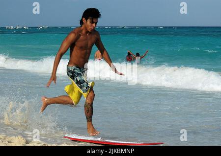 A young man playing with a surfboard on the beach on a summer day in Playa del Carmen, Mexico. Selective focus Stock Photo