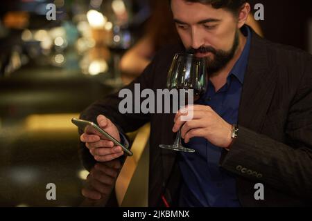 Young man texting and drinking red wine Stock Photo