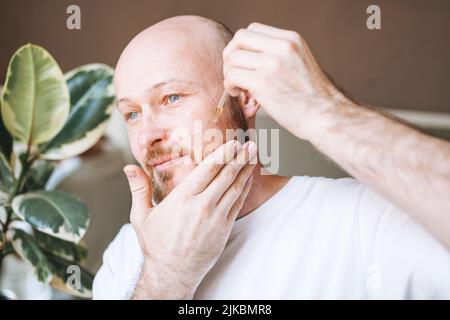 Adult handsome man with pipette with beard oil in bathroom at home Stock Photo