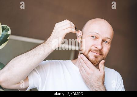 Adult handsome man with pipette with beard oil in bathroom at home Stock Photo