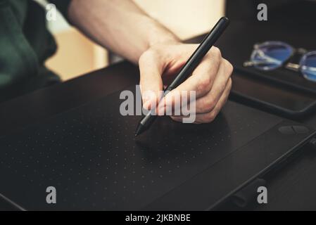 Young graphic designer man using graphic tablet on black table at home office closeup. Stock Photo